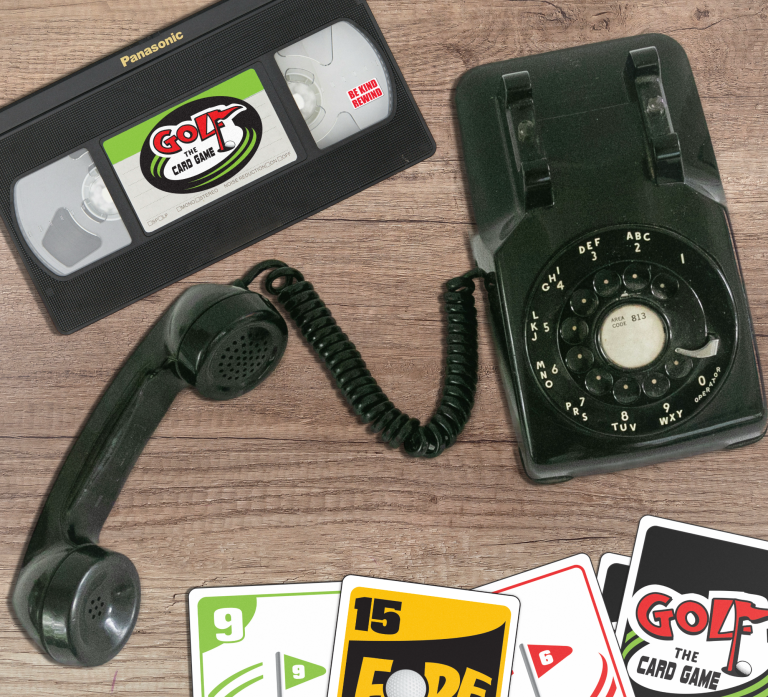 Rotary Golf the Card Game A vintage rotary phone, a VHS tape labeled "Golf the Card Game," and playing cards on a wooden surface.