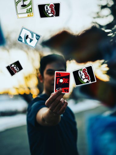 Person holding playing cards with a sunset in the background. Cards are floating around.